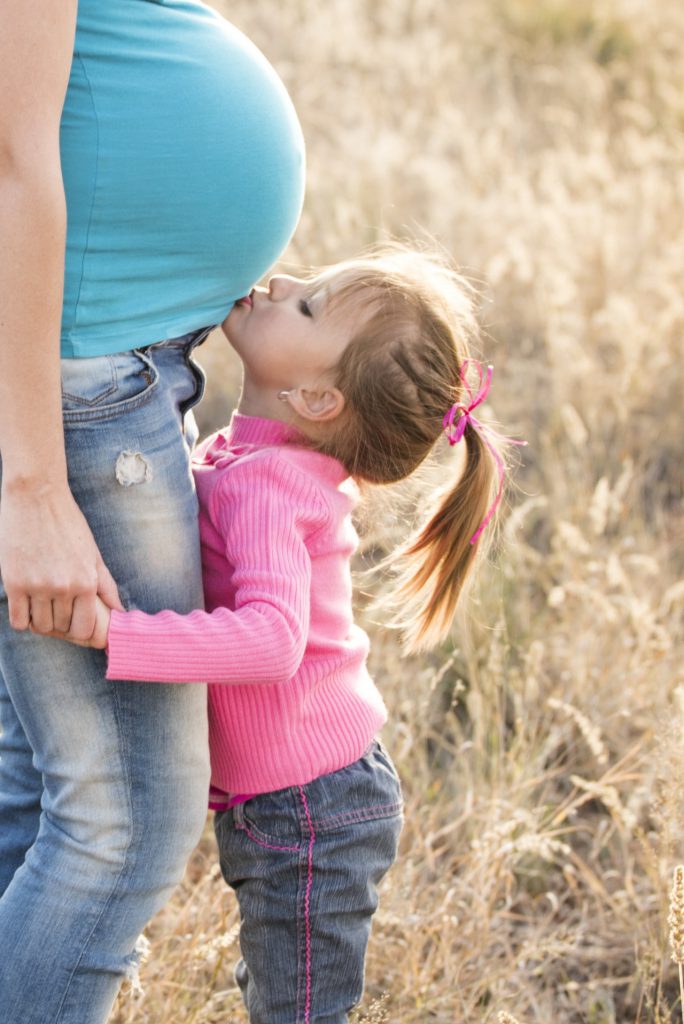 Girl in pink sweater kissing mum's tummy